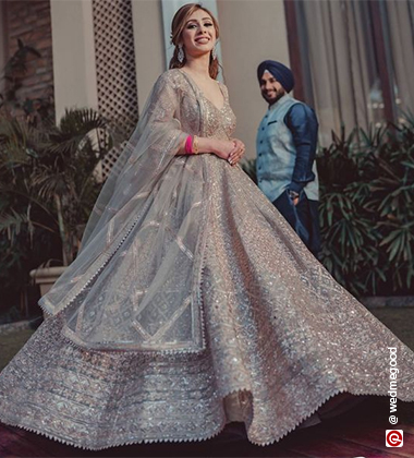 woman twirling her silver lehenga while her groom stands behind her